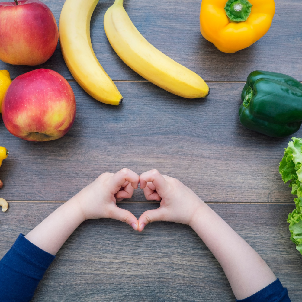 fruits and vegetables with a child making  a heart with their hands.