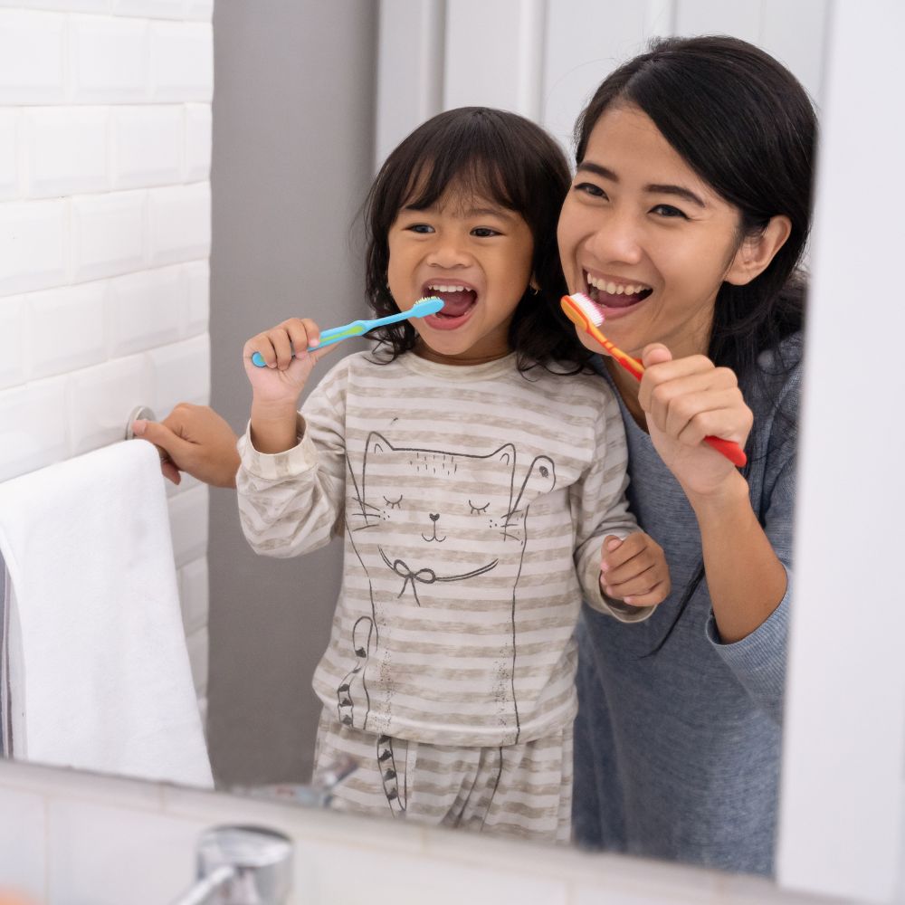 Child happily brushing her teeth with her  mom.